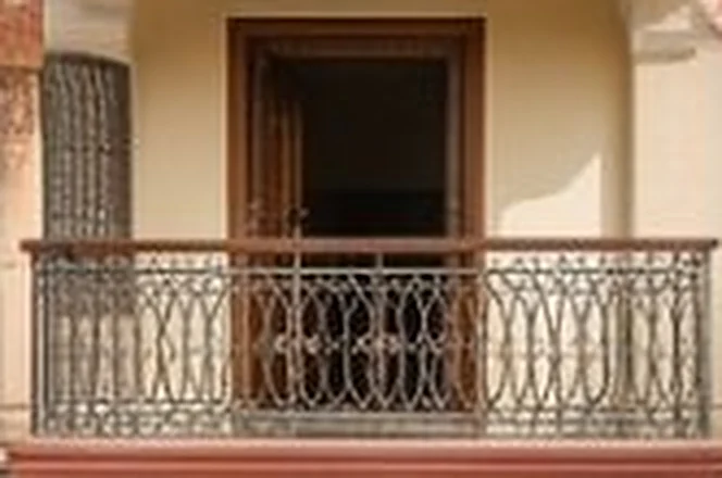 Balcony with an ornate iron railing in front of a wooden doorway
